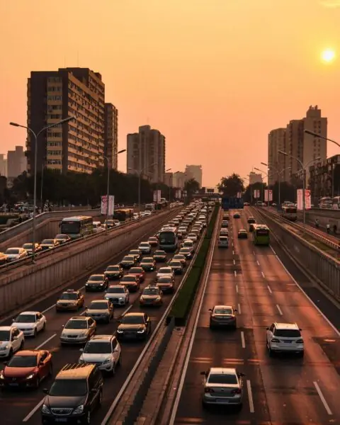 An urban highway packed with cars and trucks is illuminated by a setting sun.