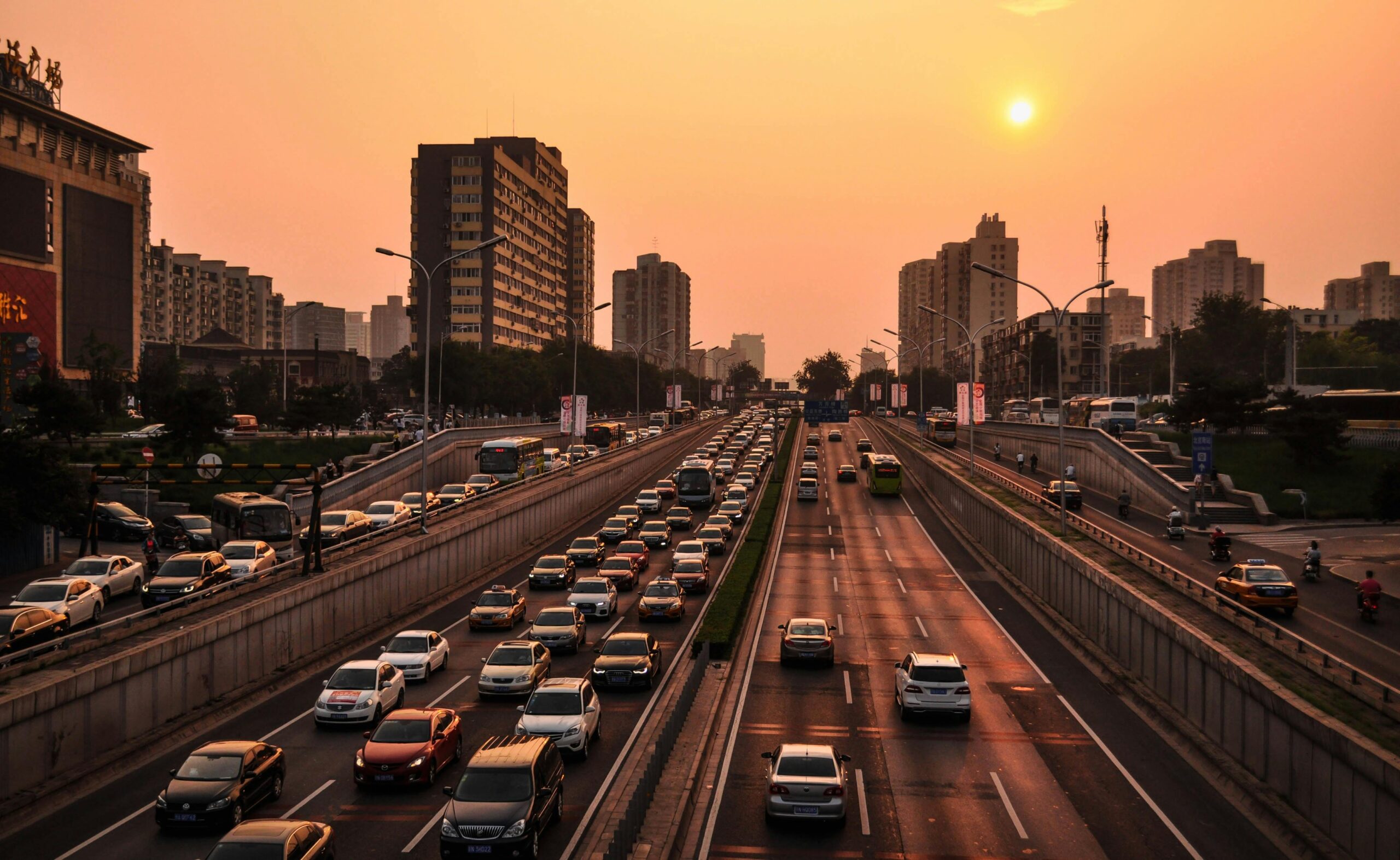 An urban highway packed with cars and trucks is illuminated by a setting sun.