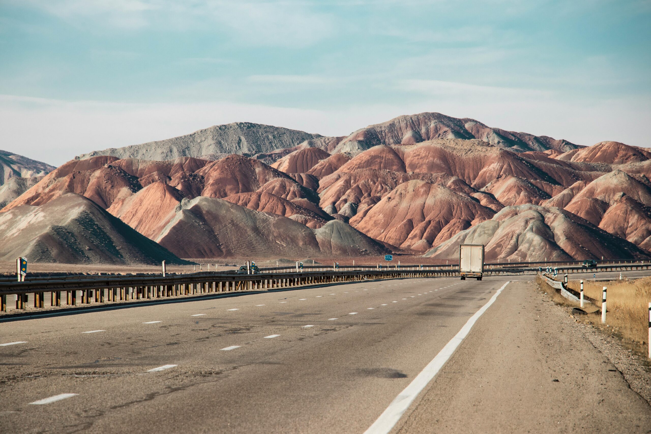 A three-lane highway carrying a semi truck through desert and dry, mountainous country.