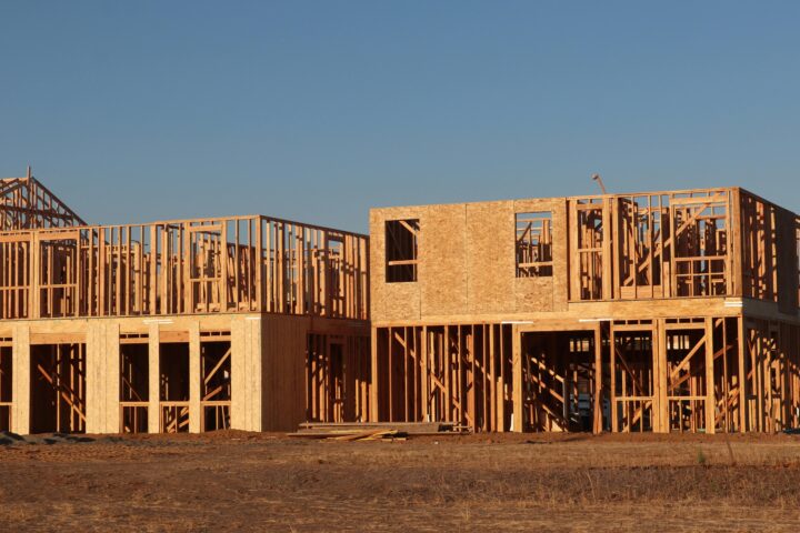 Two houses that are currently under construction on a lot underneath a blue sky.