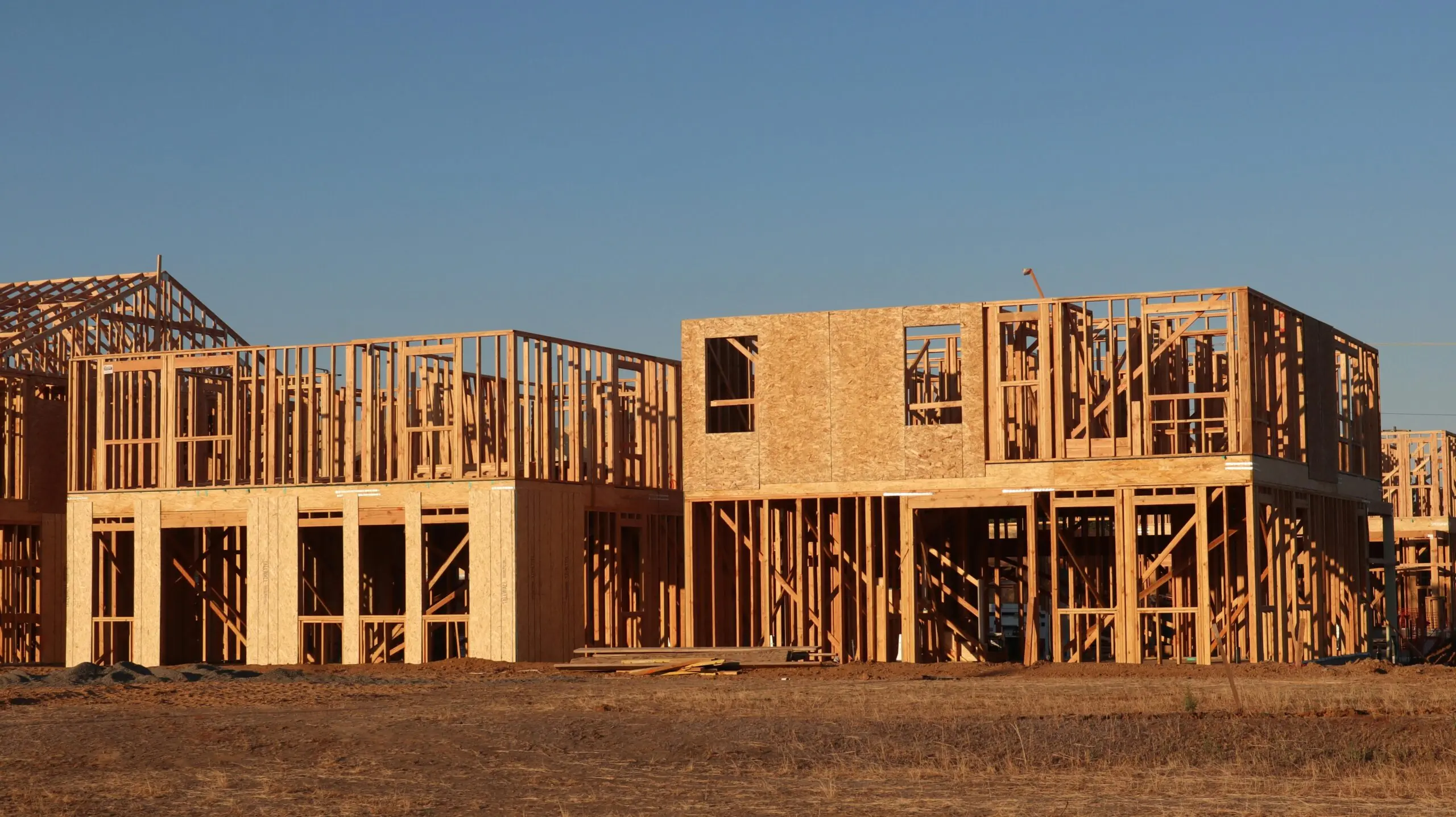 Two houses that are currently under construction on a lot underneath a blue sky.