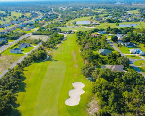 An aerial view of a golf course with other surrounding houses and structures.