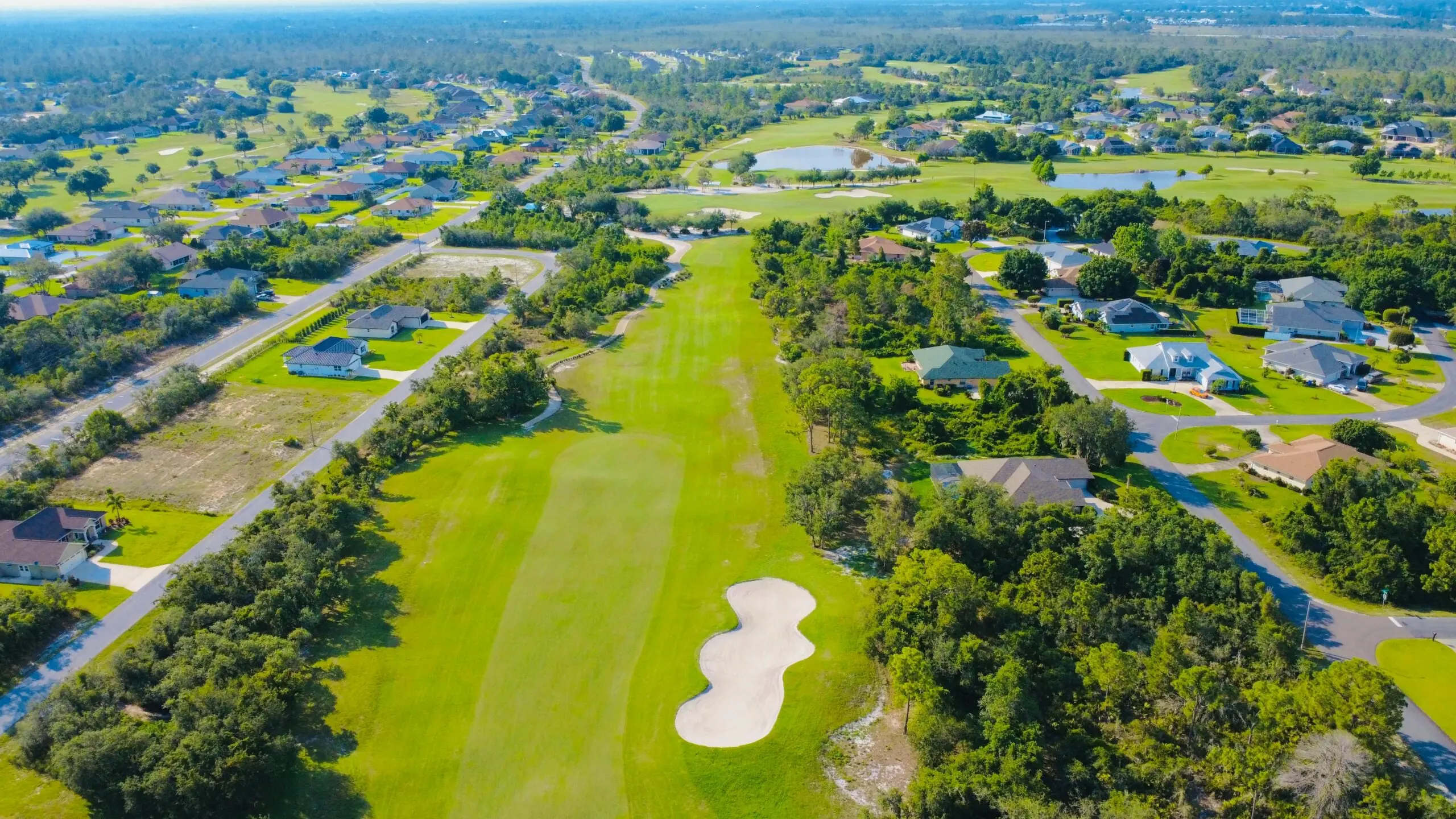 An aerial view of a golf course with other surrounding houses and structures.