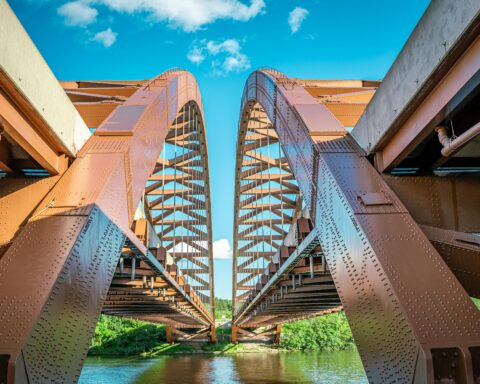 Two red bridges aligned before a blue sky and blue water below.