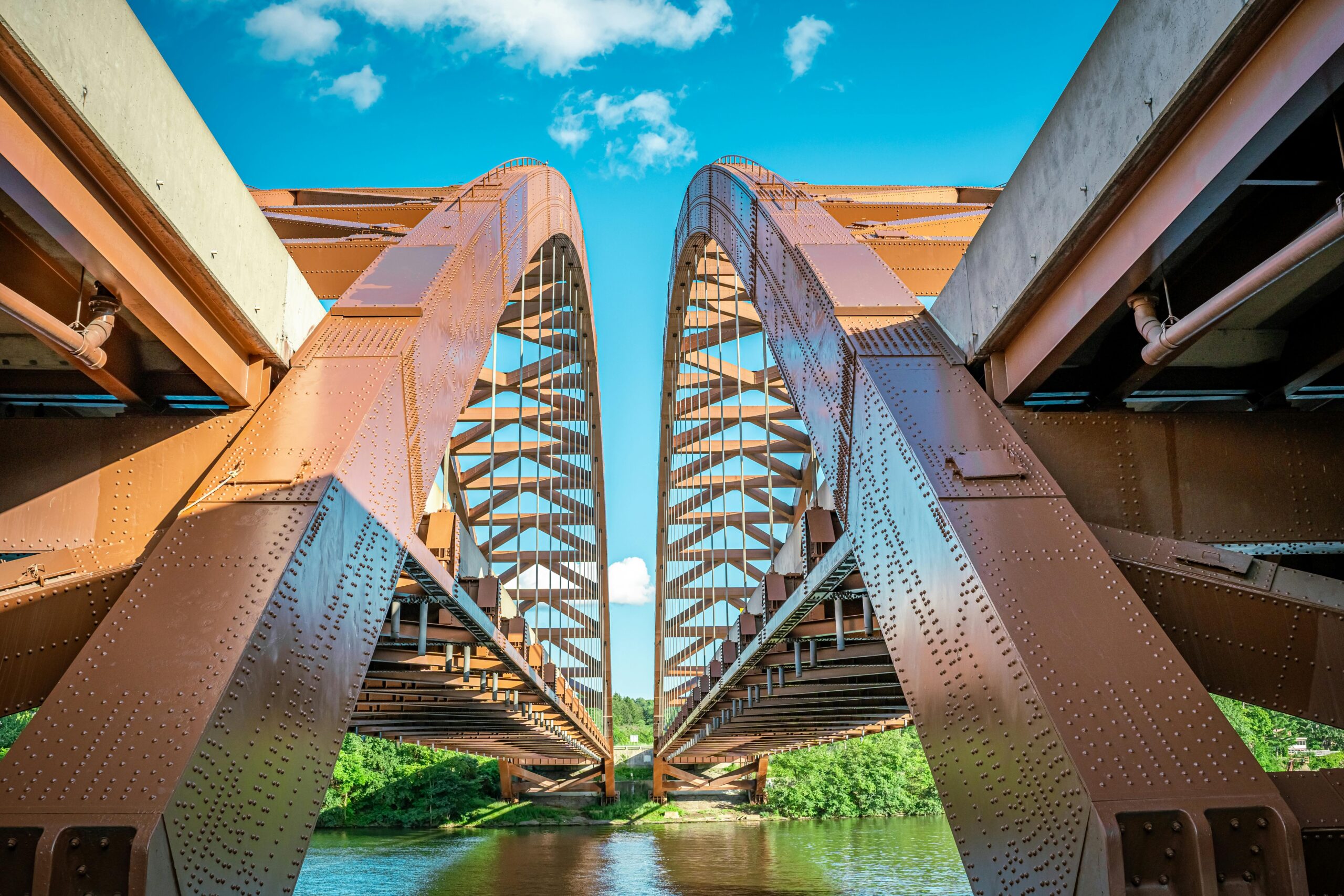 Two red bridges aligned before a blue sky and blue water below.