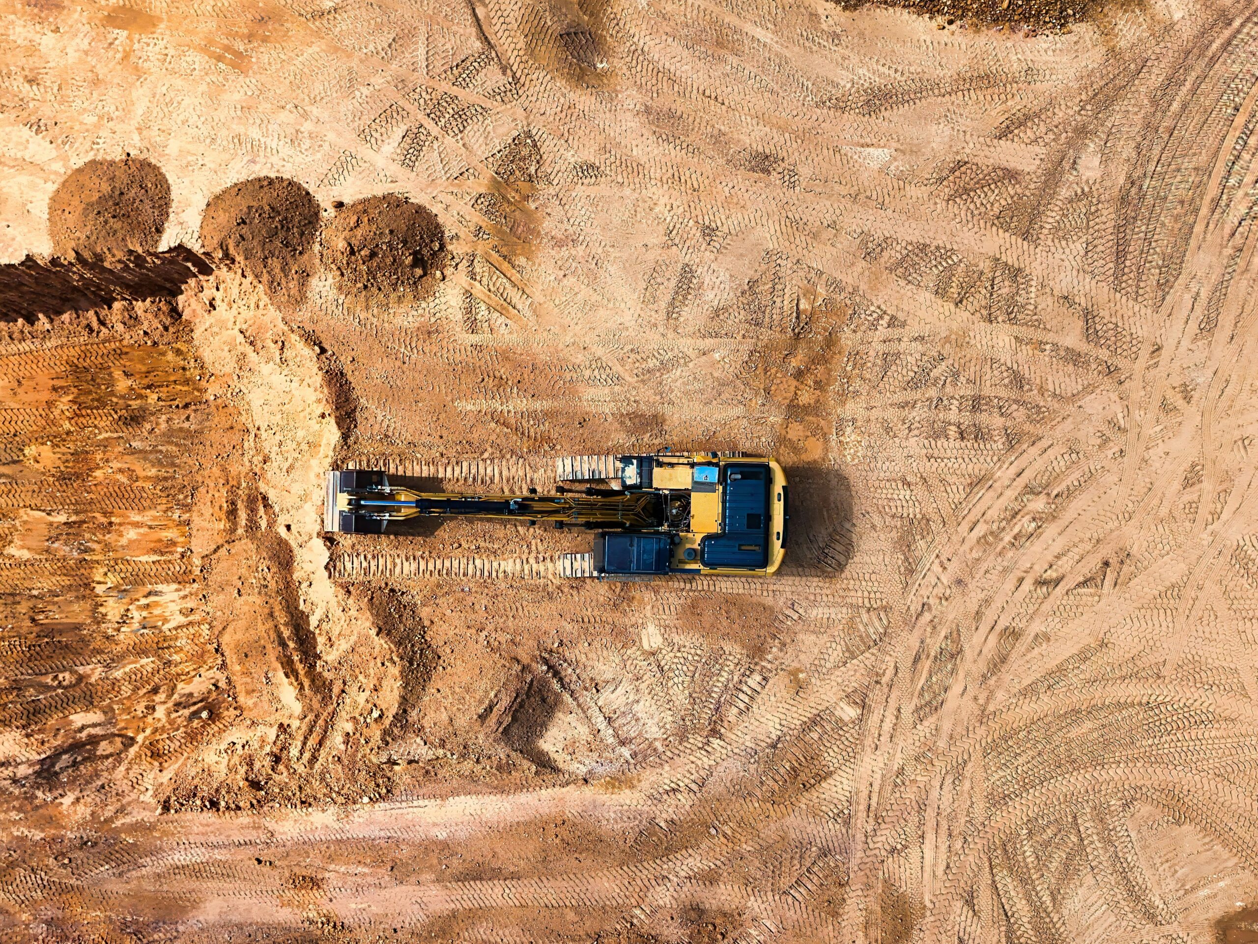An excavator on a dirt job site from an aerial perspective.