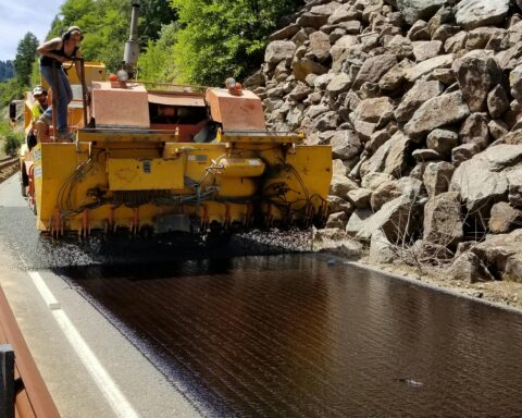 A construction vehicle repaves a winding rocky road.