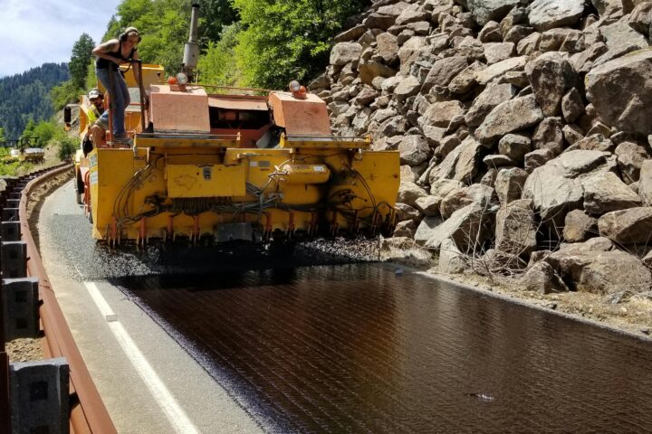 A construction vehicle repaves a winding rocky road.