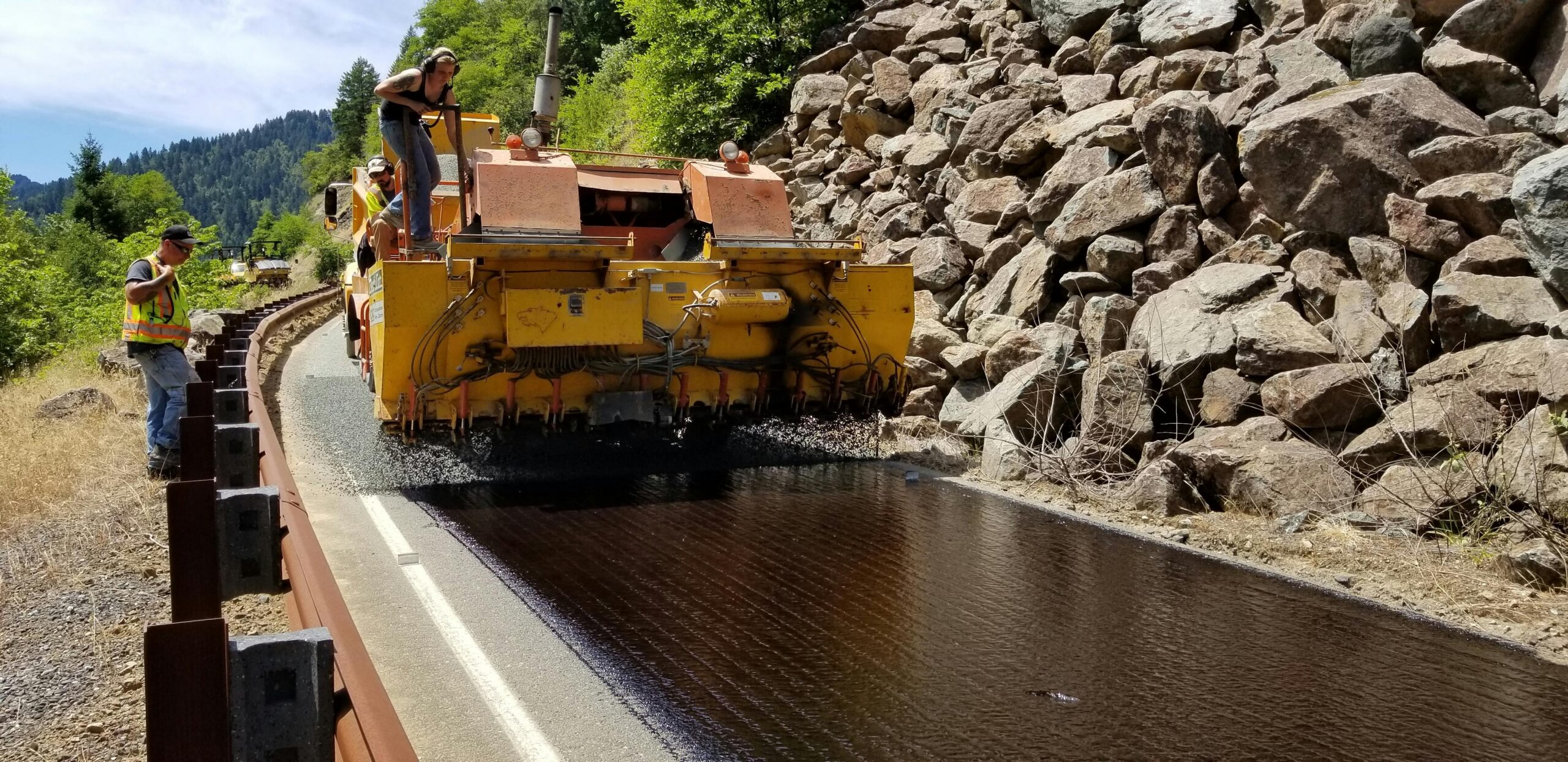 A construction vehicle repaves a winding rocky road.