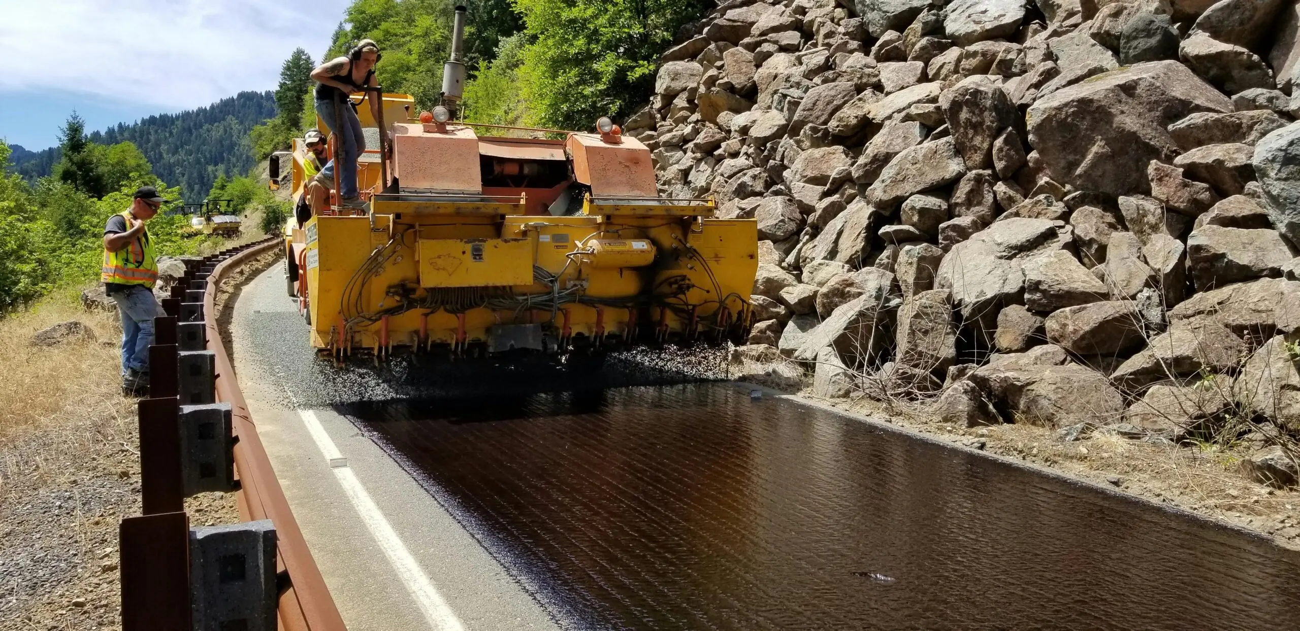 A construction vehicle repaves a winding rocky road.