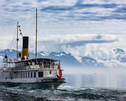 A ferry on water before snow-capped mountains.