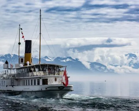 A ferry on water before snow-capped mountains.