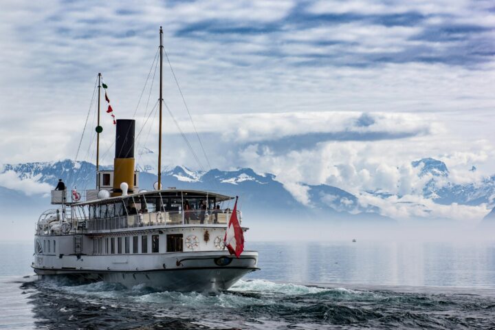 A ferry on water before snow-capped mountains.