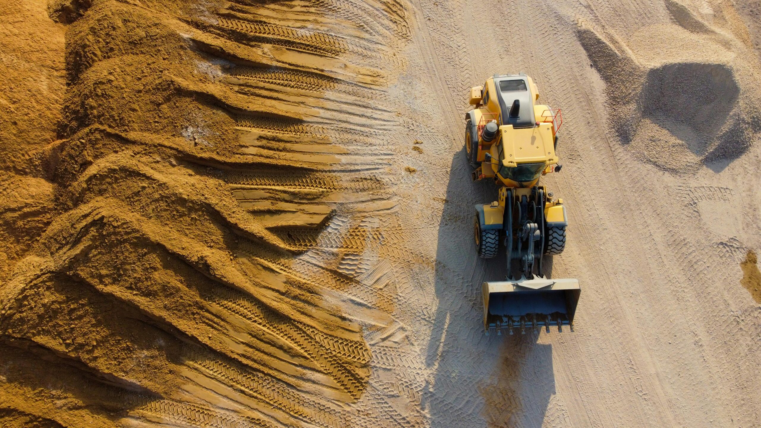 A construction vehicle on a work site next to a pile of dirt from an aerial perspective.