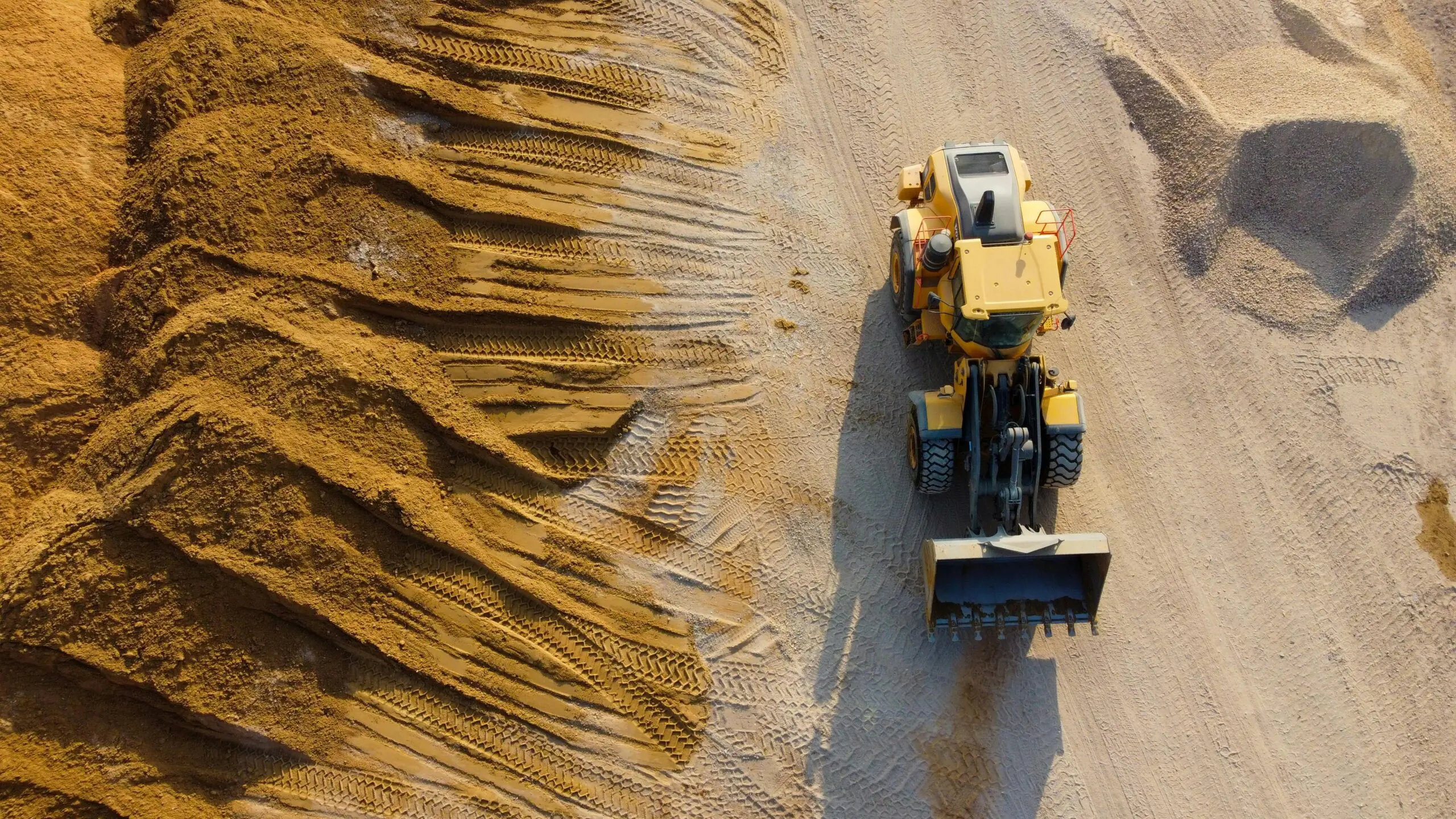 A construction vehicle on a work site next to a pile of dirt from an aerial perspective.