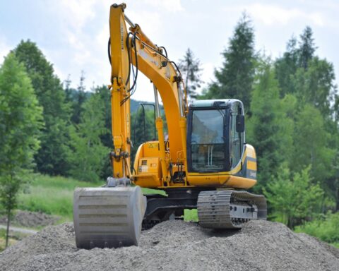 An excavator on a dirt pile before green trees.