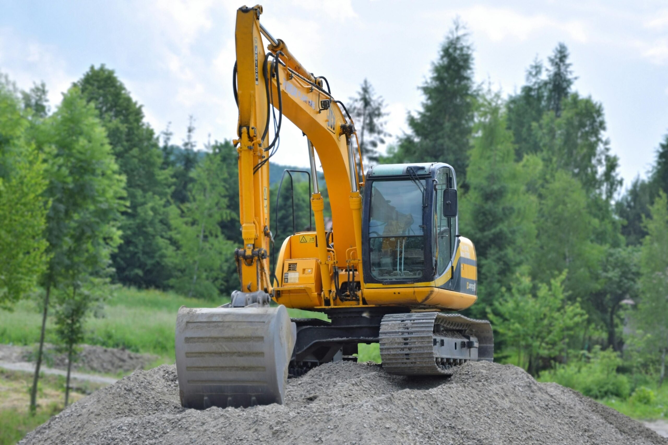 An excavator on a dirt pile before green trees.