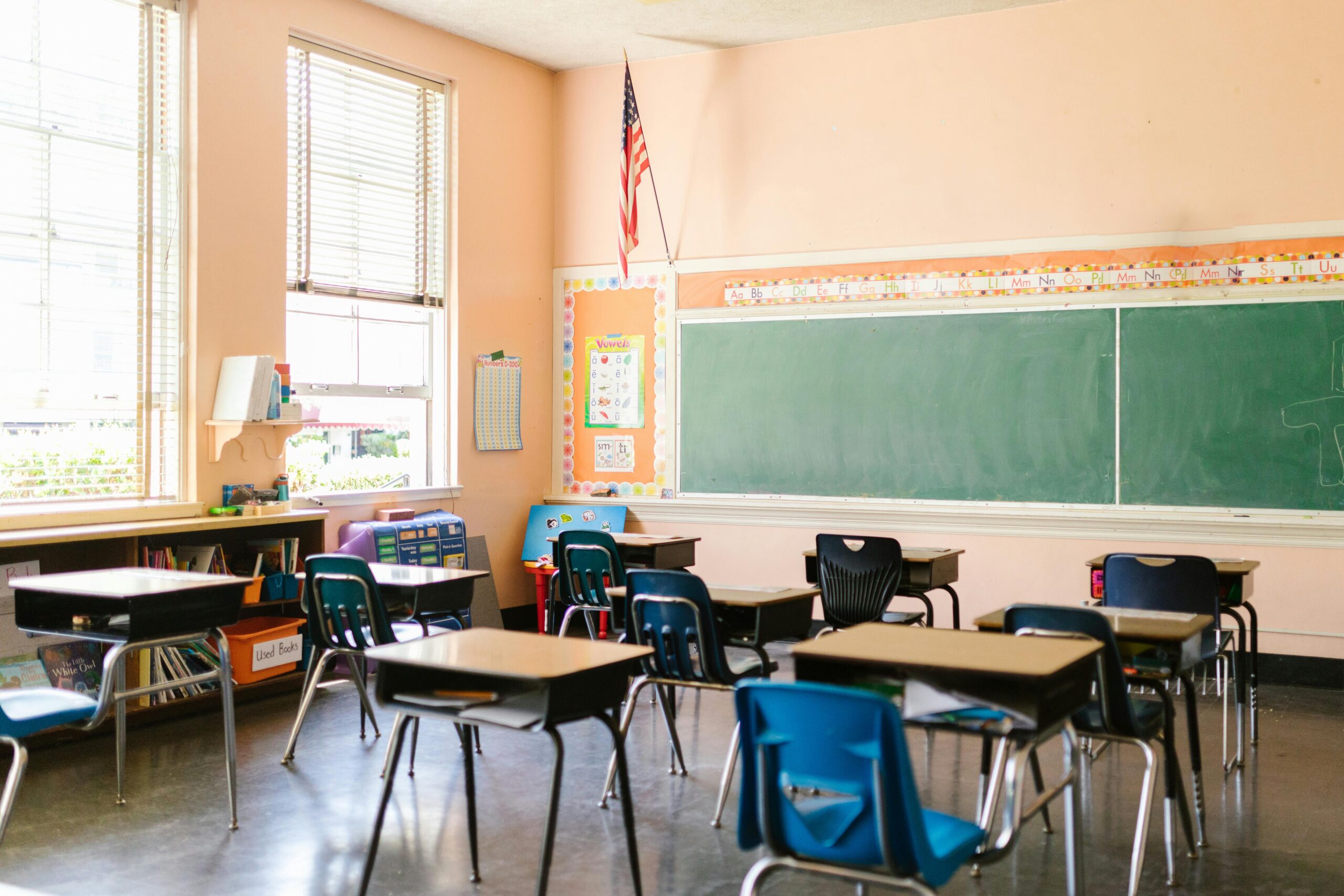 An elementary school classroom with chairs and desks before a chalkboard.