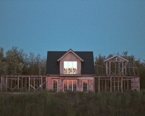 A house next to two housing developments before a forest in the dark.
