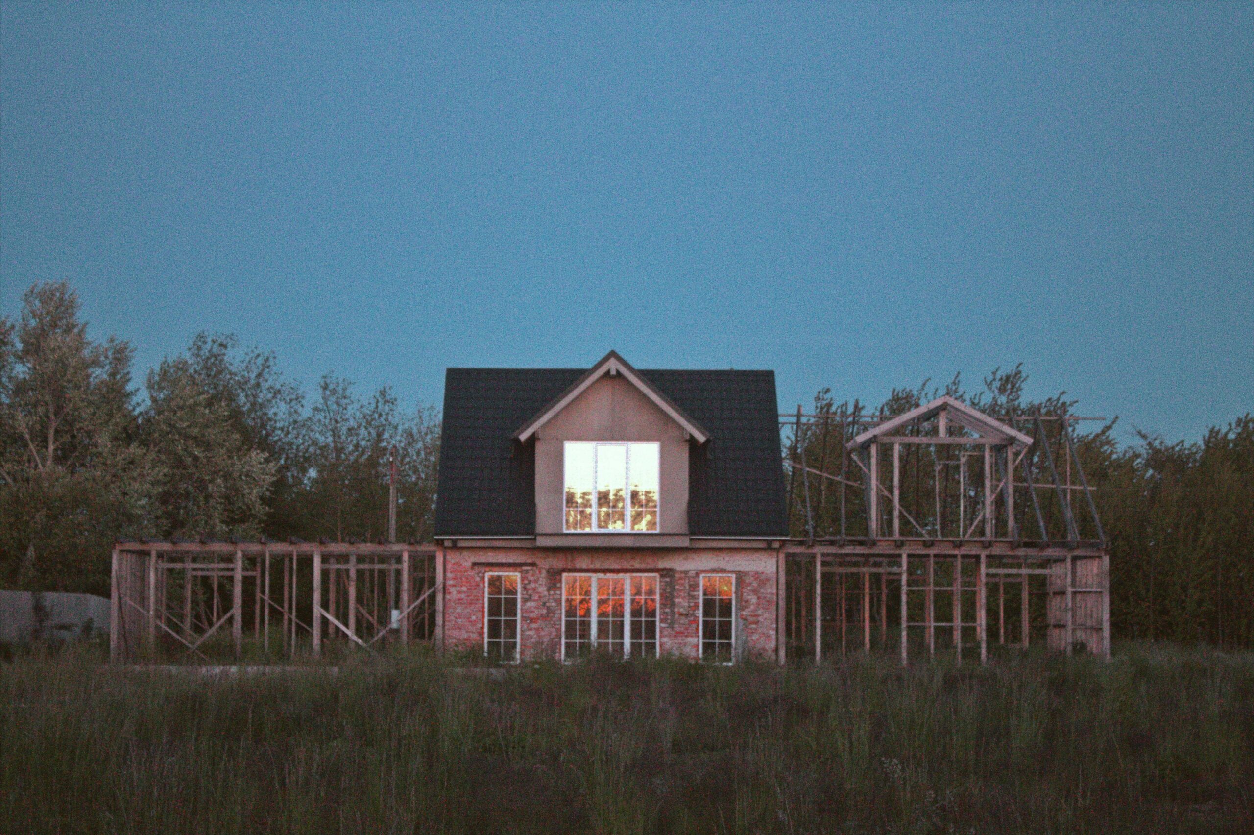 A house next to two housing developments before a forest in the dark.