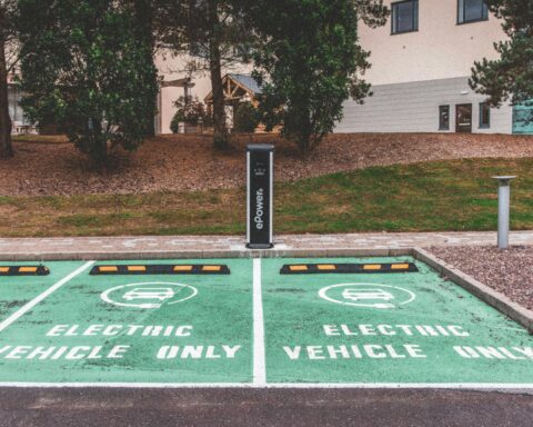 Two parking spots reserved for electric vehicles only next to a dual charging station nearby grass and some trees.
