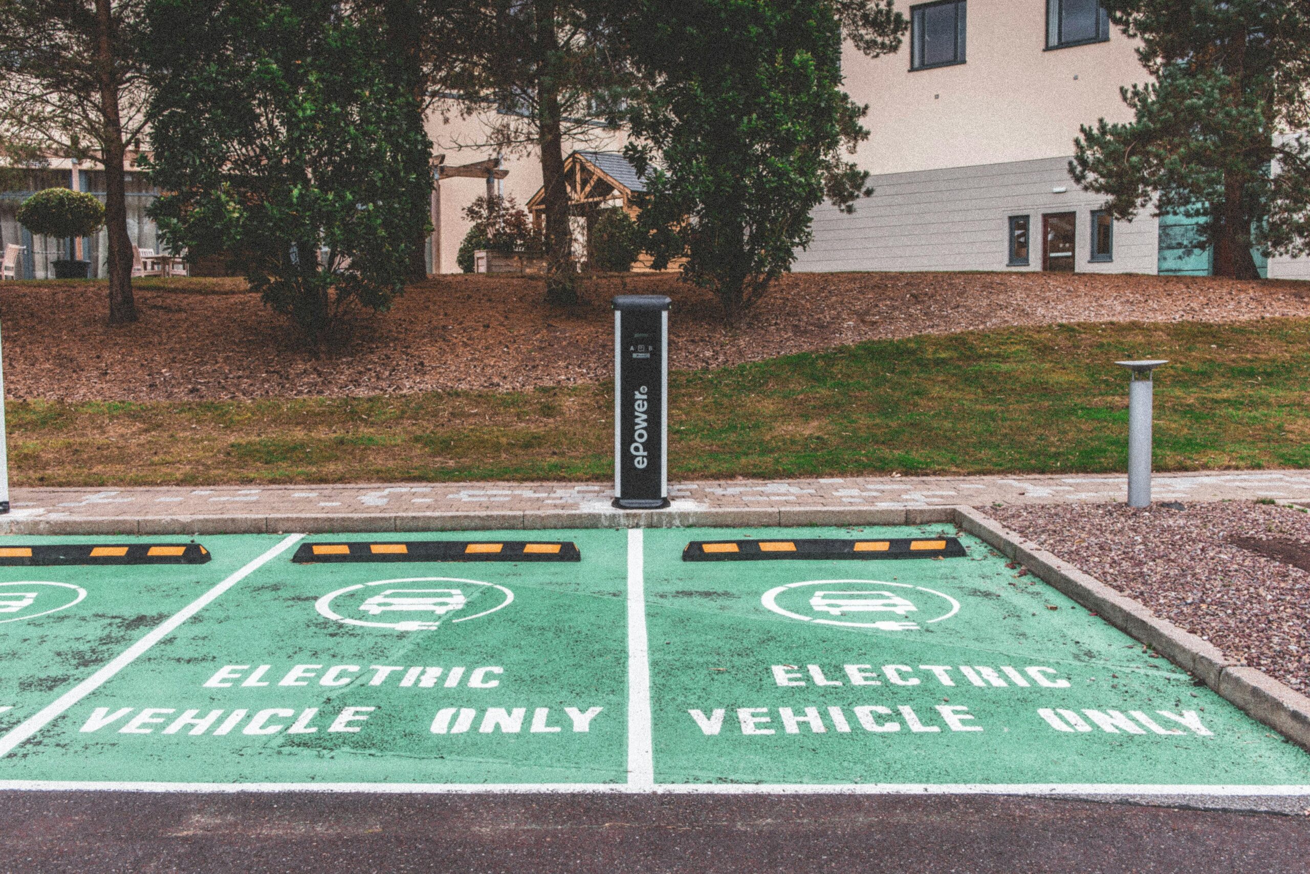 Two parking spots reserved for electric vehicles only next to a dual charging station nearby grass and some trees.