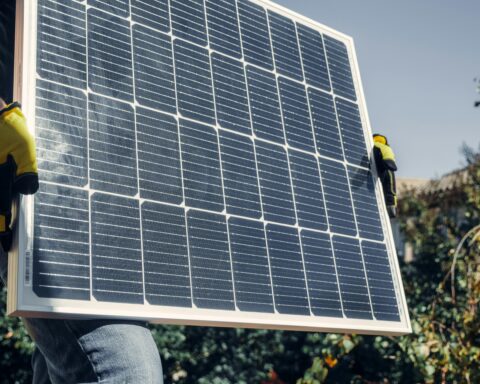 A construction worker carries a solar panel for installation.