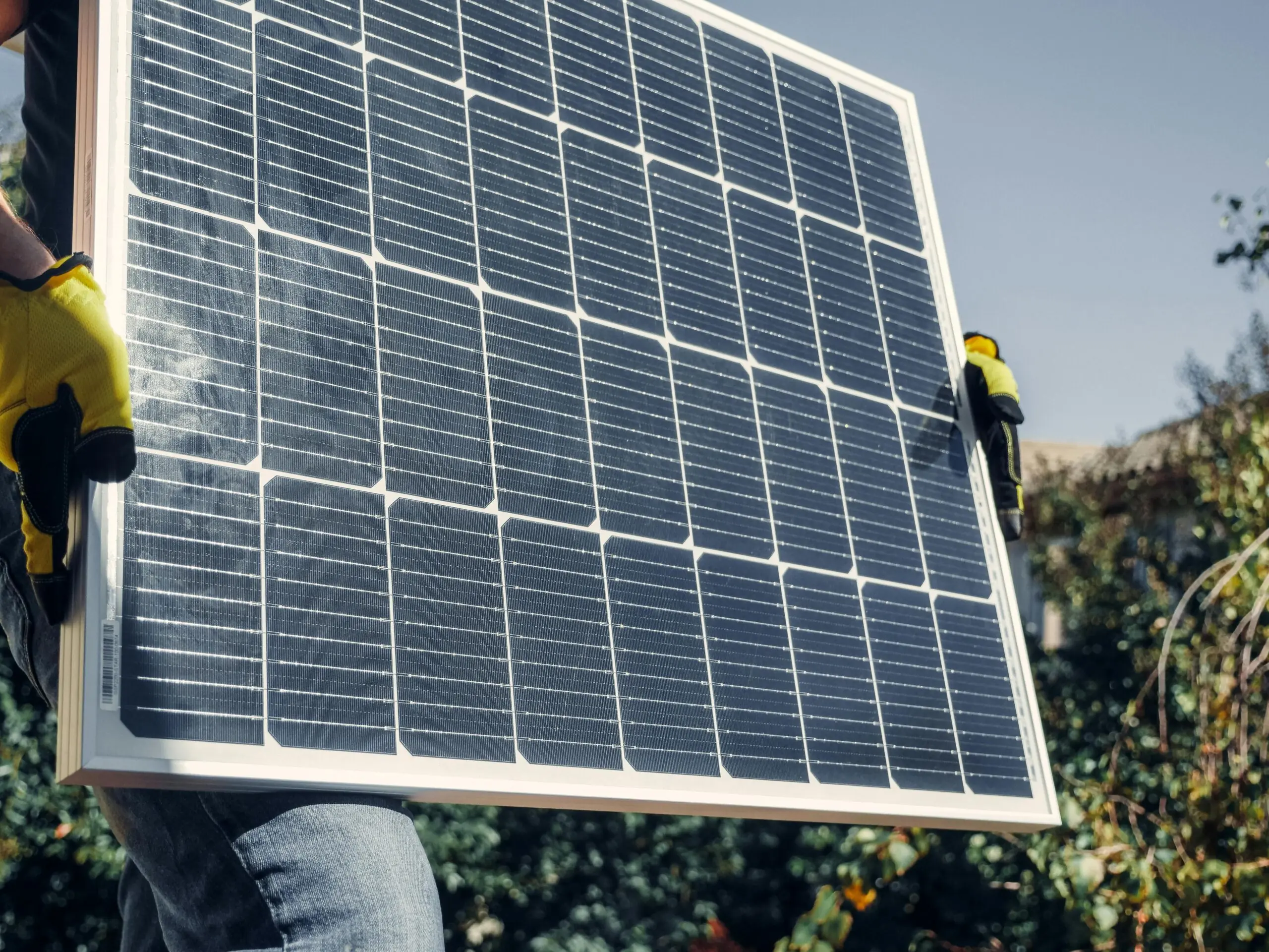 A construction worker carries a solar panel for installation.