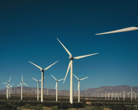 Wind turbines in an empty field before a blue sky and distant hills.