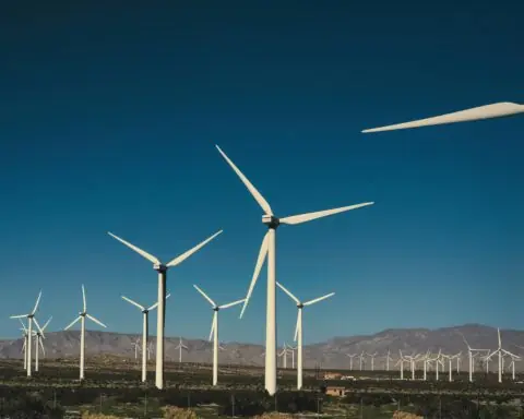 Wind turbines in an empty field before a blue sky and distant hills.