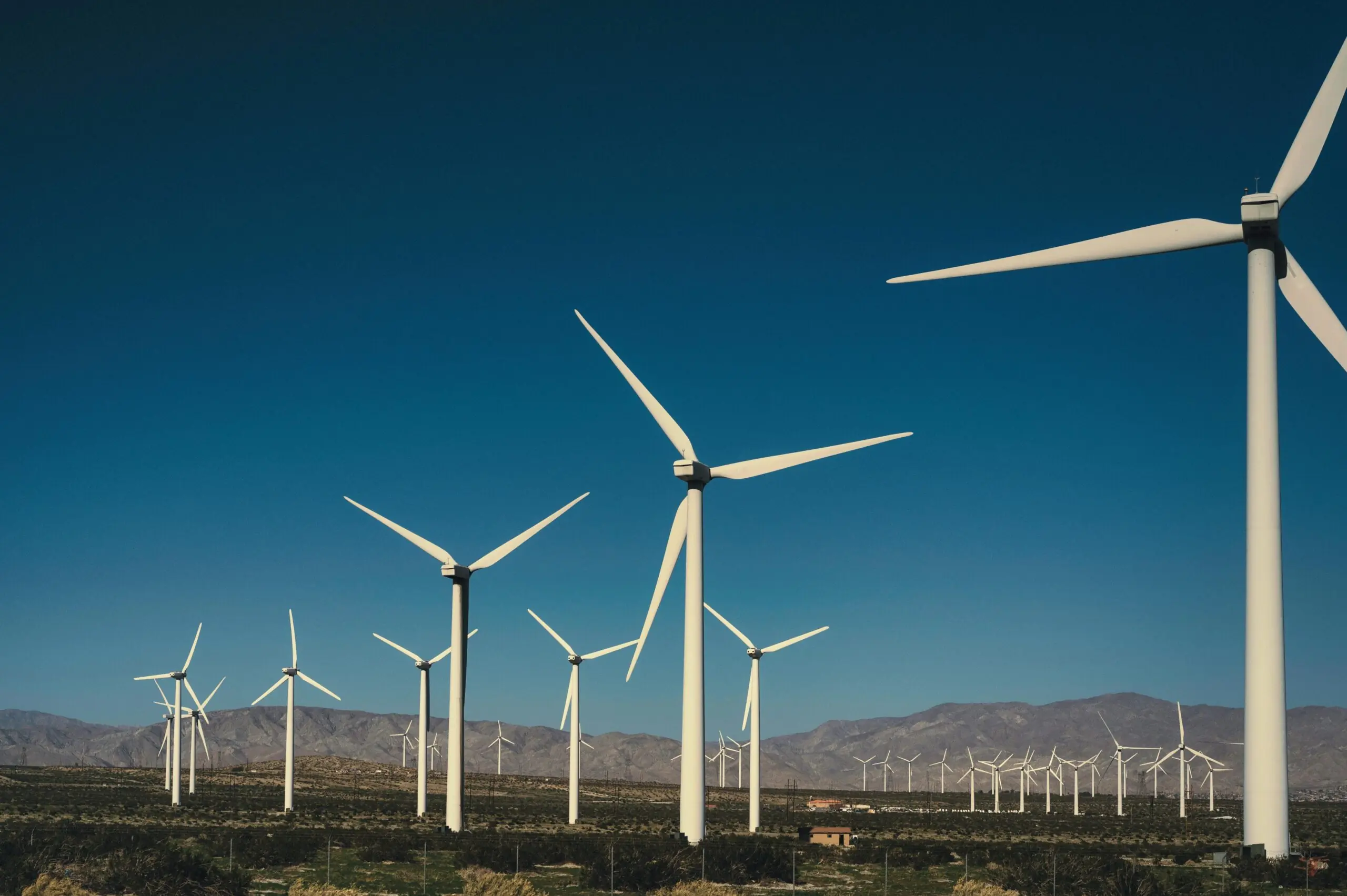 Wind turbines in an empty field before a blue sky and distant hills.