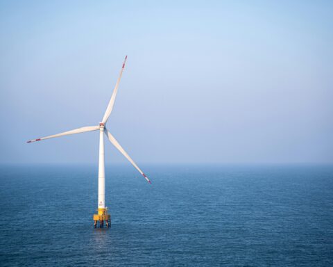 A solo wind turbine in the middle of a body of water.