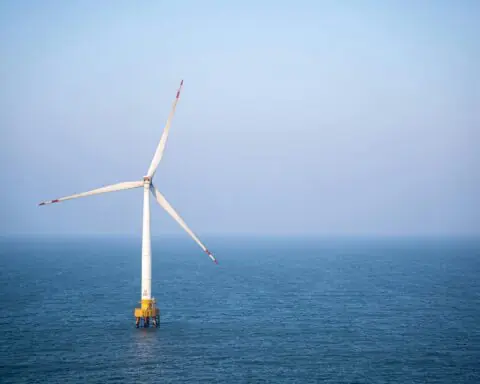 A solo wind turbine in the middle of a body of water.