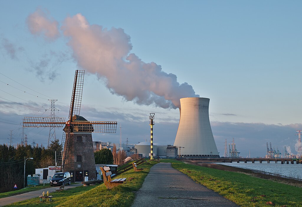 A nuclear power plant in Belgium alongside a nearby windmill and road.
