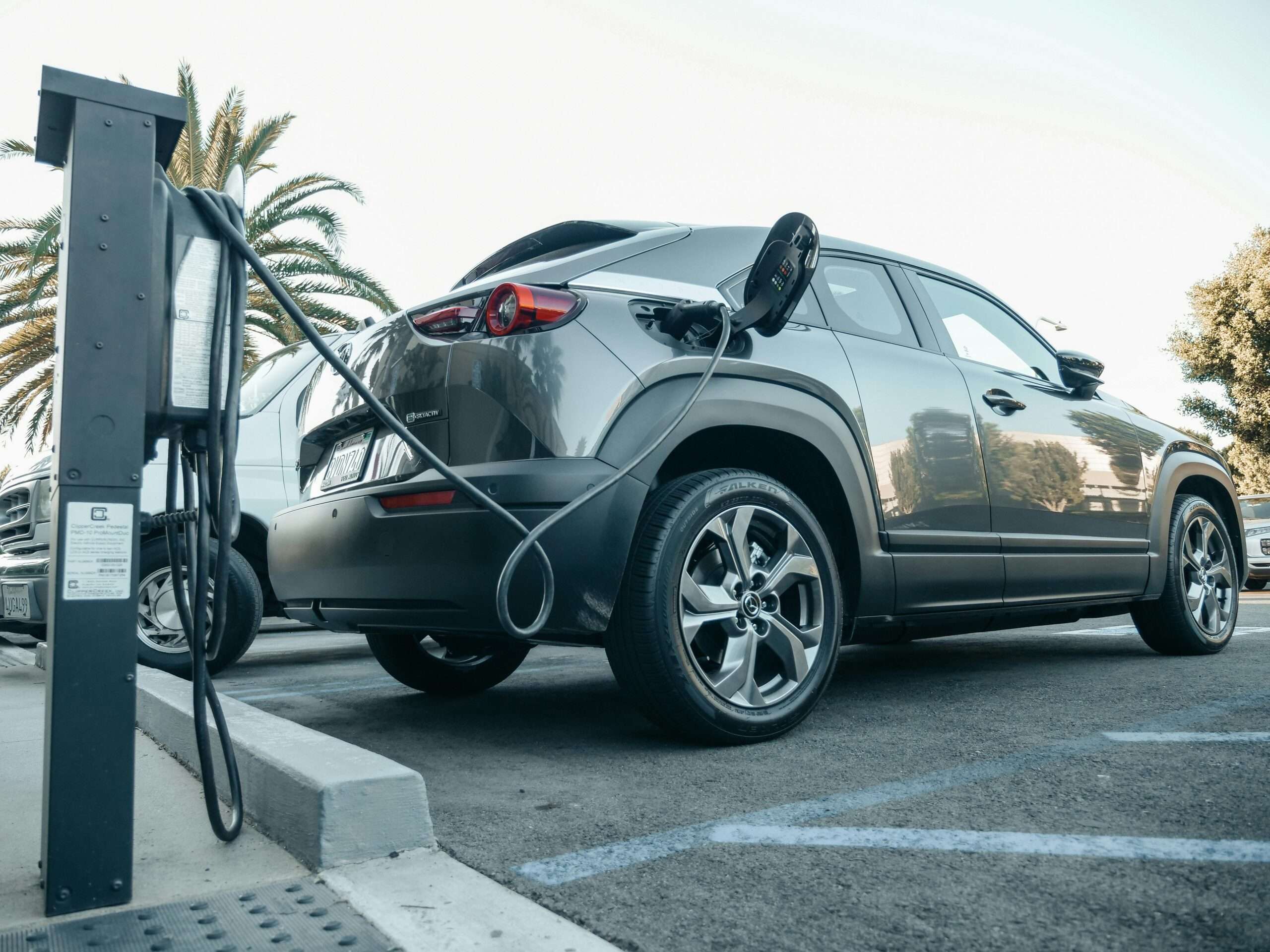 An electric car in a parking lot connected to a charging station before a bright sky.