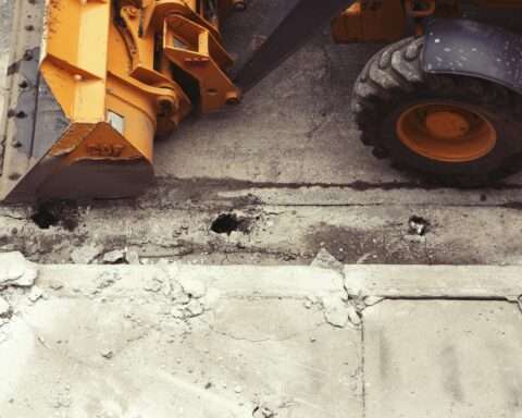 A bulldozer alongside a cracked sidewalk curb from above.