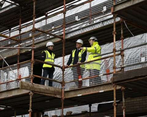 Construction workers stand along scaffolding while constructing a building.