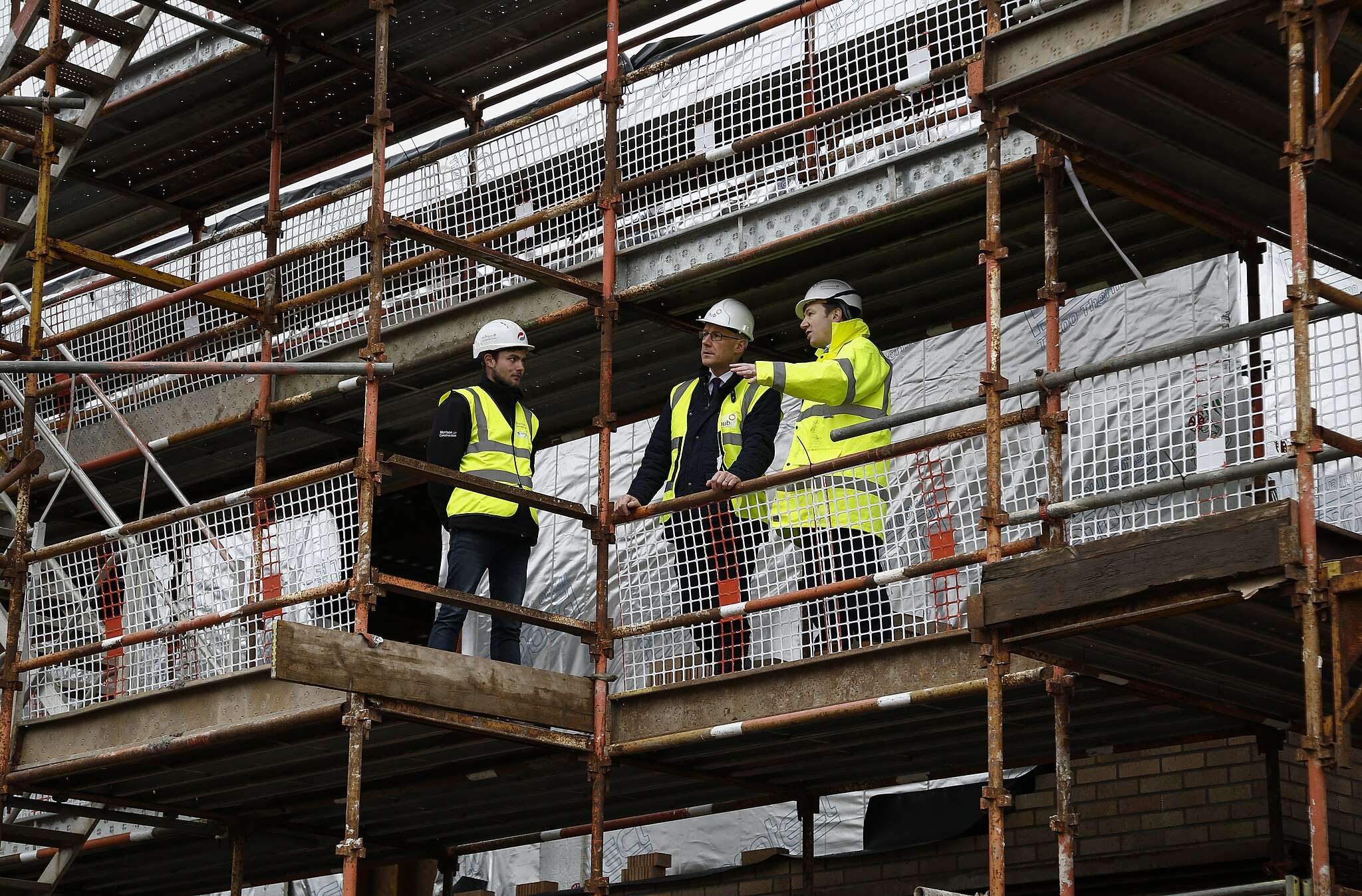 Construction workers stand along scaffolding while constructing a building.