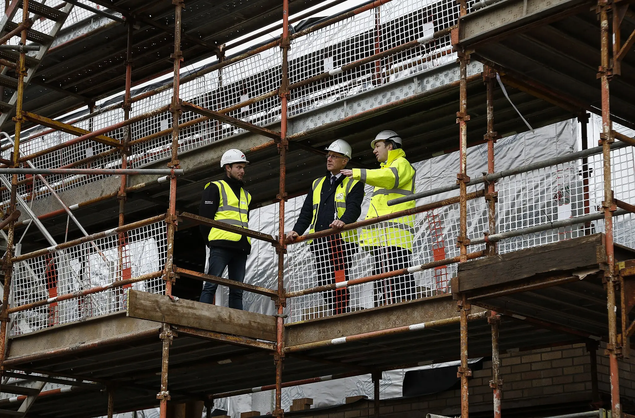 Construction workers stand along scaffolding while constructing a building.