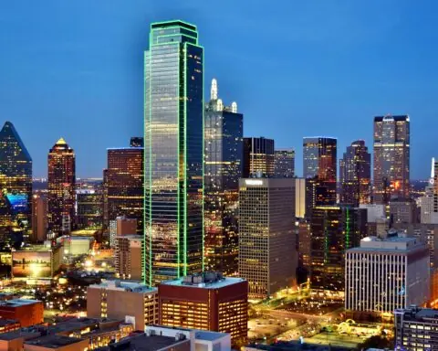The Dallas city skyline before a dark blue sky.