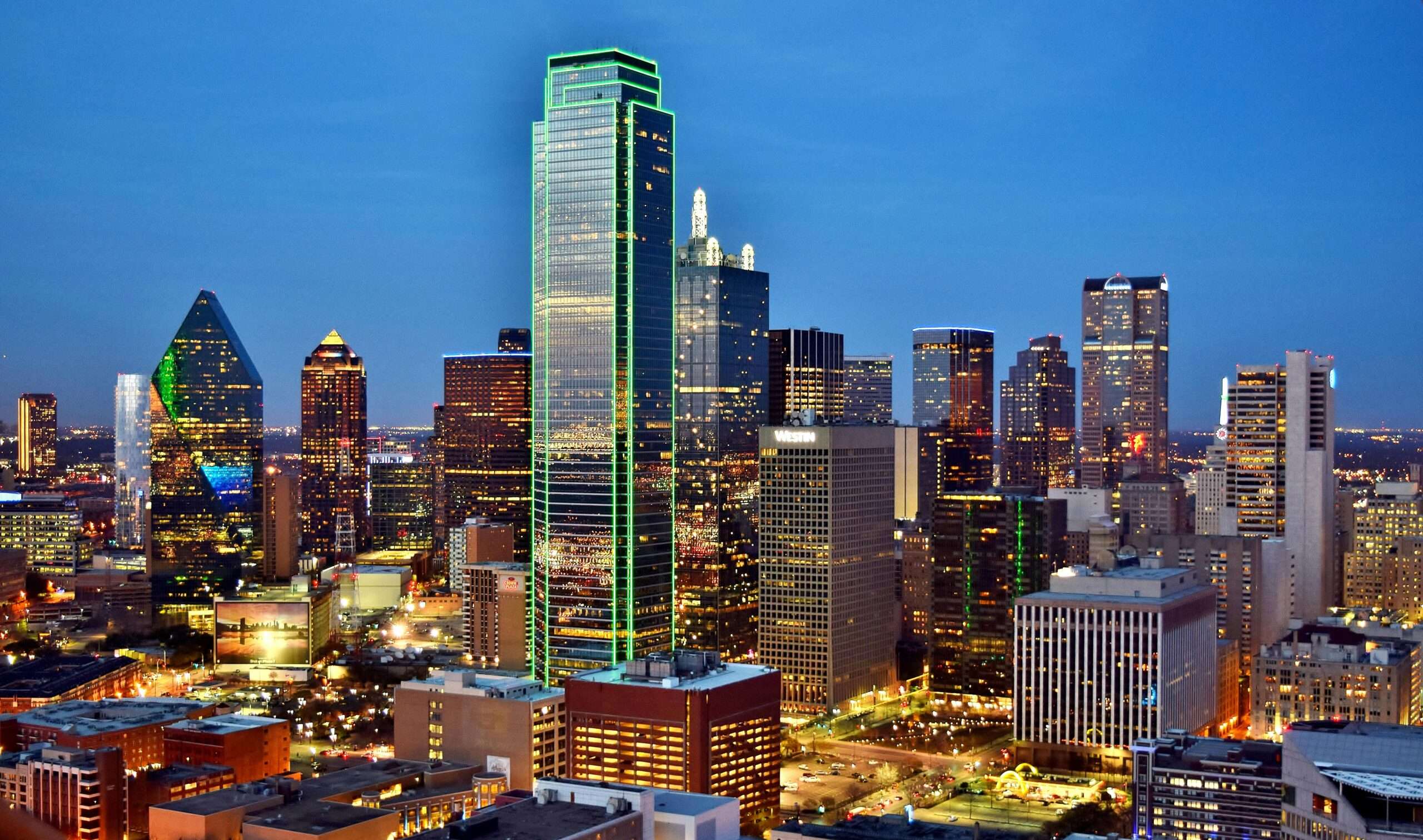 The Dallas city skyline before a dark blue sky.