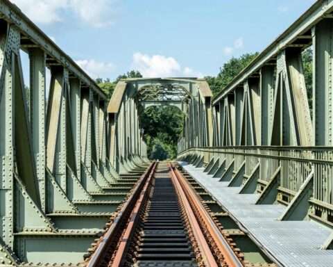 A rusty rail with brown tracks leading across a green bridge.