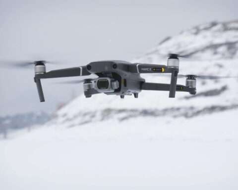 A black drone floating above snowy ground before a white background.