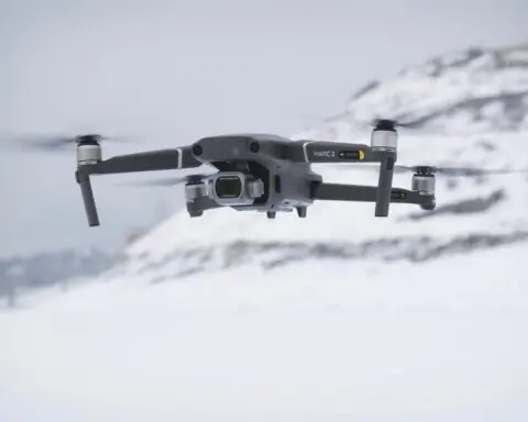 A black drone floating above snowy ground before a white background.