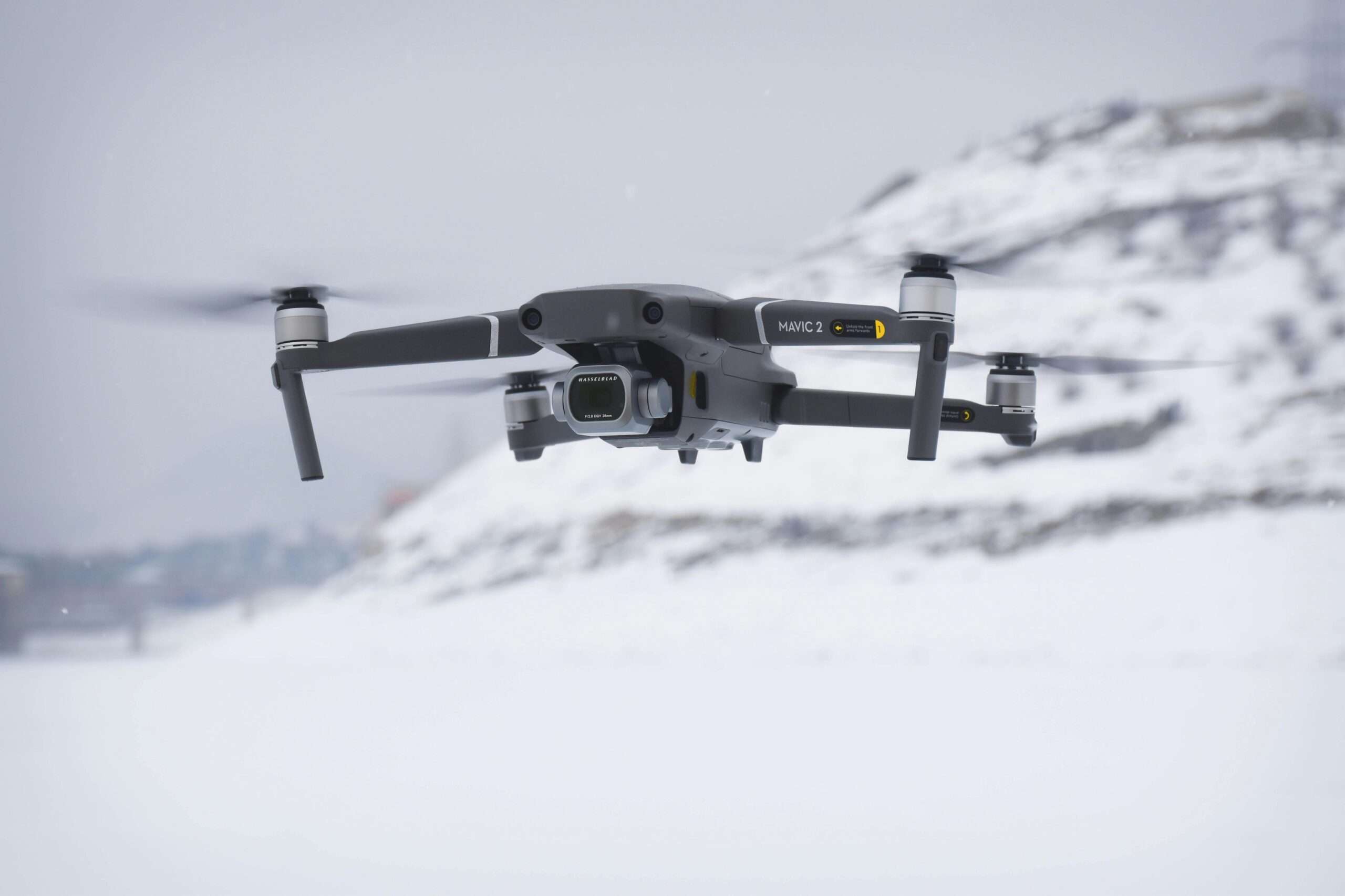 A black drone floating above snowy ground before a white background.