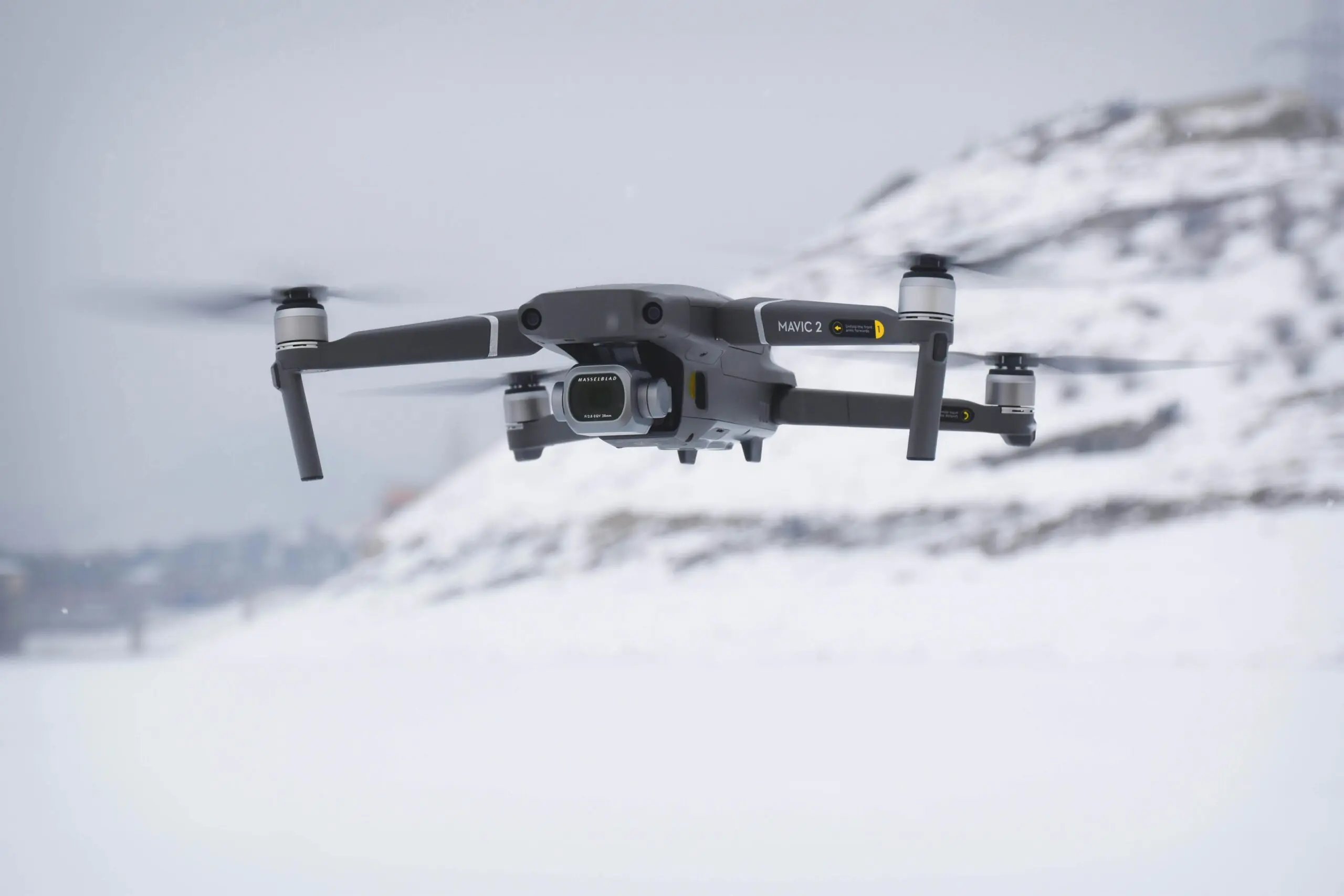 A black drone floating above snowy ground before a white background.