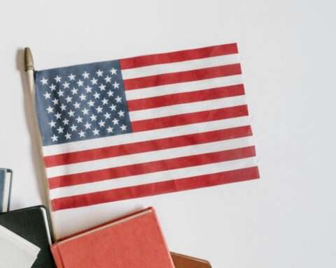 An American flag next to school books before a white background.