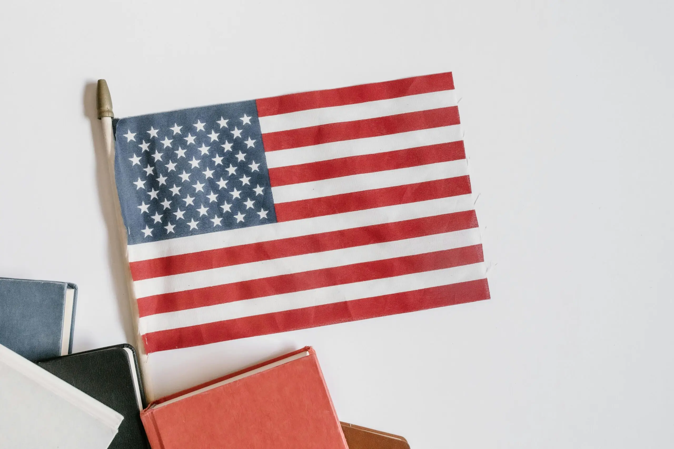 An American flag next to school books before a white background.