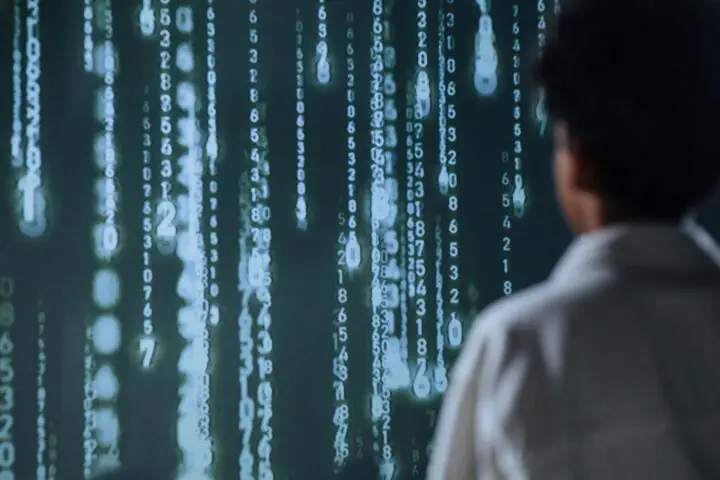 A man stands before a digitized wall with dropping code streaks.