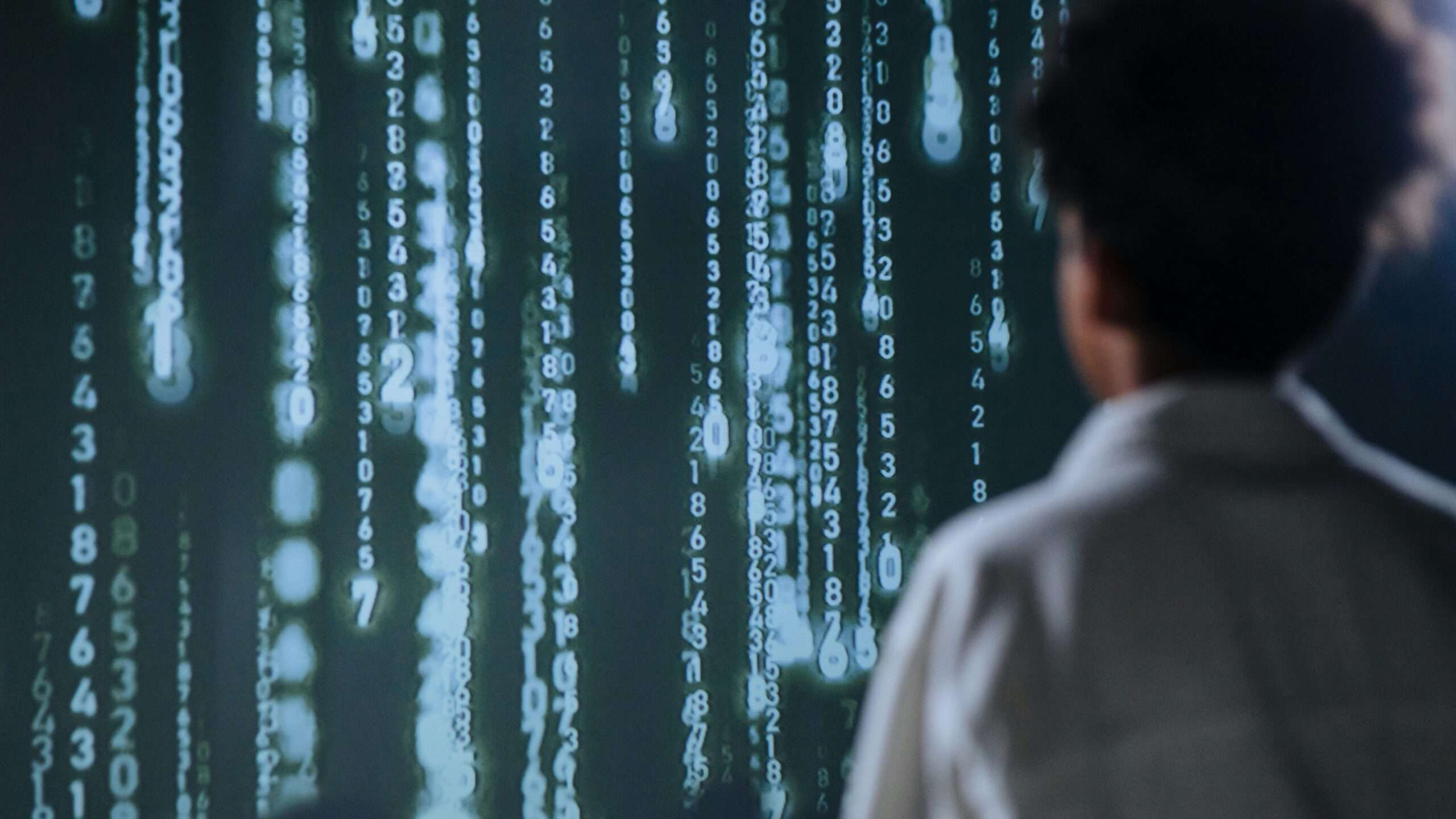 A man stands before a digitized wall with dropping code streaks.